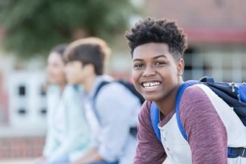 A kid in a backpack smiling into the camera