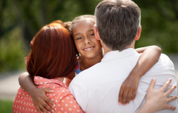 Two adults hugging a child